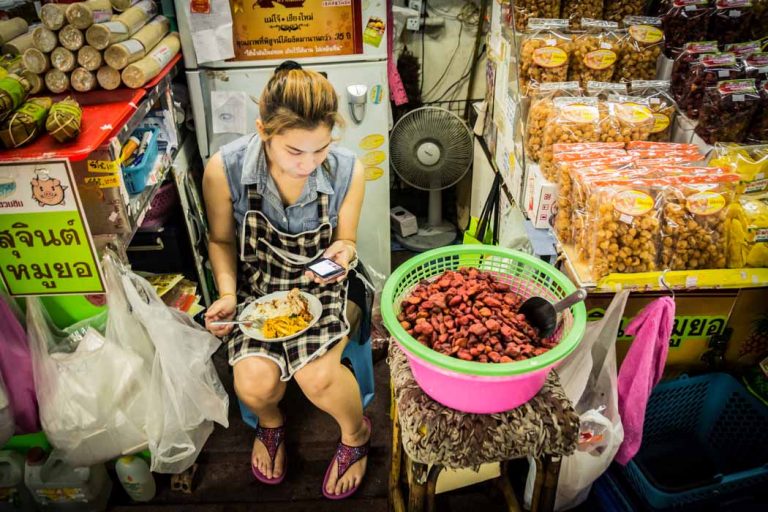 A girl reading her mobile while eating in a food stall in Worarot Market. Chiang Mai, Thailand.